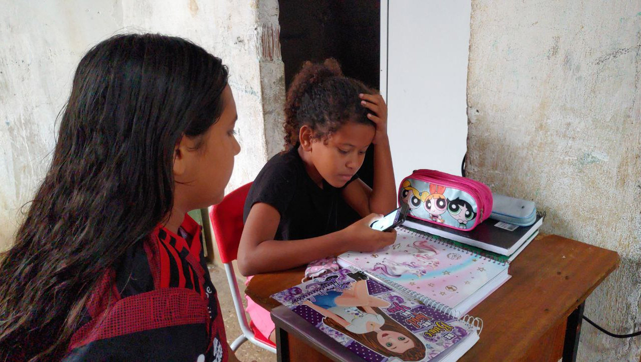   Menina de 9 anos divide celular com o irmão e uma amiga para conseguirem estudar. Maria Mel é aluna do quarto ano do ensino fundamental da Escola Municipal João Niceras de Morais, no Sítio Pedra Branca. Desde 2020, início da pandemia do coronavírus, a menina tem acompanhado as aulas por um pequeno celular doado pela professora, através do aplicativo whatsapp, pois o aparelho não suporta o download do google meet (aplicativo de reuniões por onde as aulas remotas estão sendo ministradas). O equipamento ainda é compartilhado com a amiga Letícia Aparecida, de 12 anos, que cursa a mesma série, e com o irmão José Messias, de 8 anos, que cursa o segundo ano do ensino fundamental.
