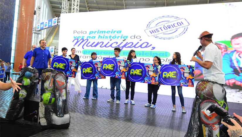 Imagem 1 -  O Programa de Apoio ao Estudante (PAE), teve seu edital lançado e oferecerá 5 mil bolsas com valores mensais entre R$ 200 e R$ 300 aos estudantes. Também foram prorrogadas as inscrições dos programas de intercâmbio Partiu Brasil e Mossoró para o Mundo, além da reforma de 10 escolas e creches. Durante o evento, houve entrega de materiais esportivos, apresentação do Prêmio IDEB e anúncio do Projeto de Lei do Passe Livre Estudantil, que prevê transporte gratuito para alunos de todas as redes de ensino do município.